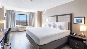 Habitación de hotel con una cama grande, un escritorio y una silla. Hay una ventana con cortinas, un cuadro en la pared y una lámpara en la mesita de noche.