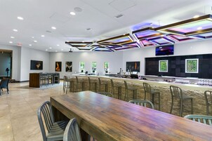 A modern bar area with a long wooden table and bar stools, a counter with a TV, and artwork on the walls.