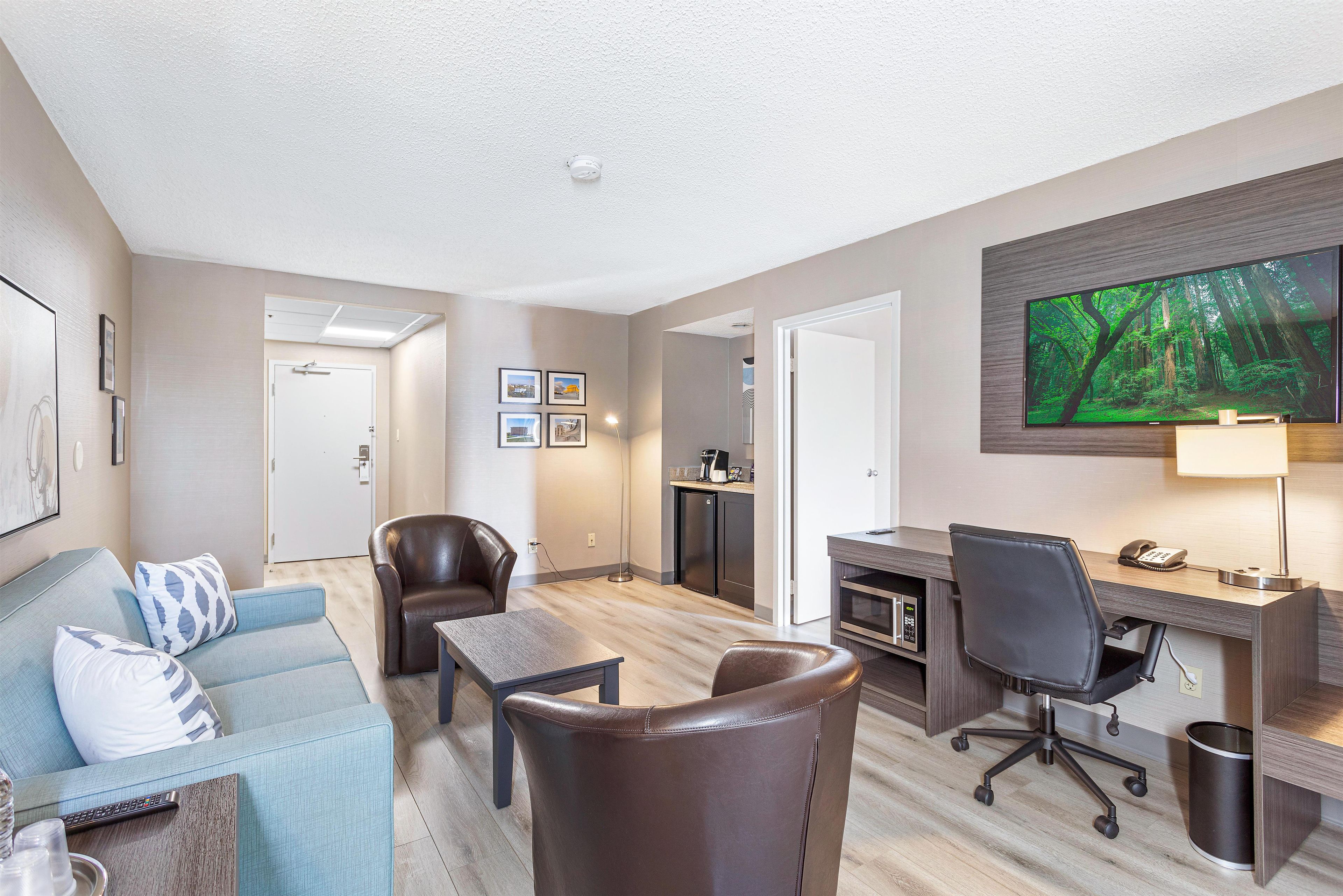 A modern living room with a sofa, chairs, a desk, and a television.
