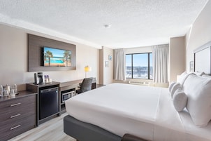 Habitación de hotel con una cama grande, un escritorio con cafetera, un televisor montado en la pared y una ventana con cortinas.