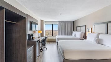 Habitación de hotel con dos camas, un escritorio, una silla, un televisor y un ventanal grande.