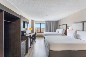 Habitación de hotel con dos camas, un escritorio, una silla, un televisor y un ventanal grande.