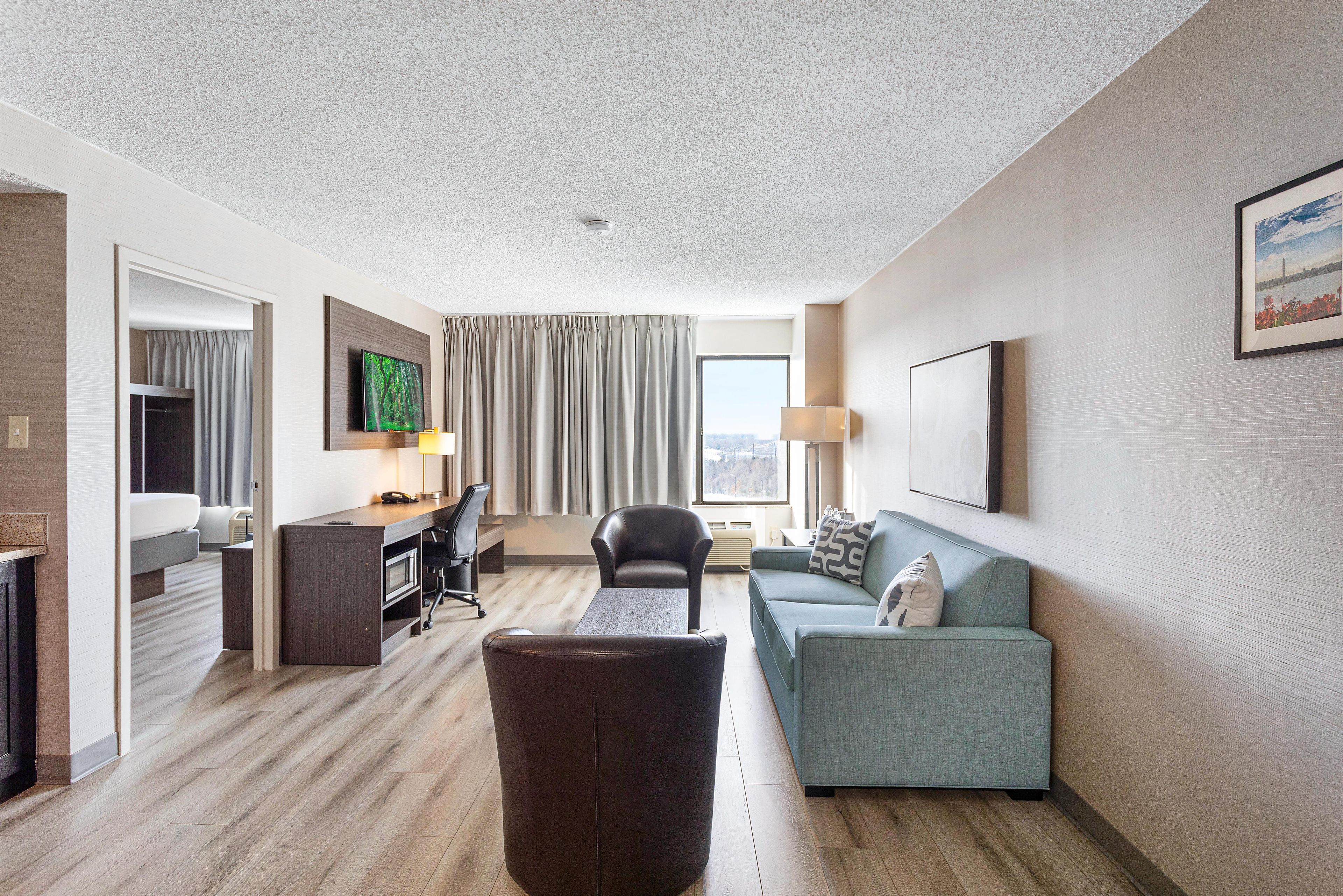 A hotel room with a desk, a sofa, a TV, and a large window.