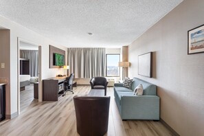 A hotel room with a desk, a sofa, a TV, and a large window.