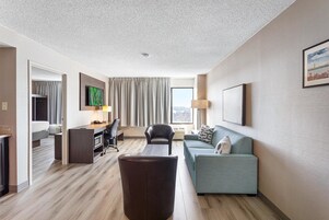 A hotel room with a desk, a sofa, a TV, and a large window.