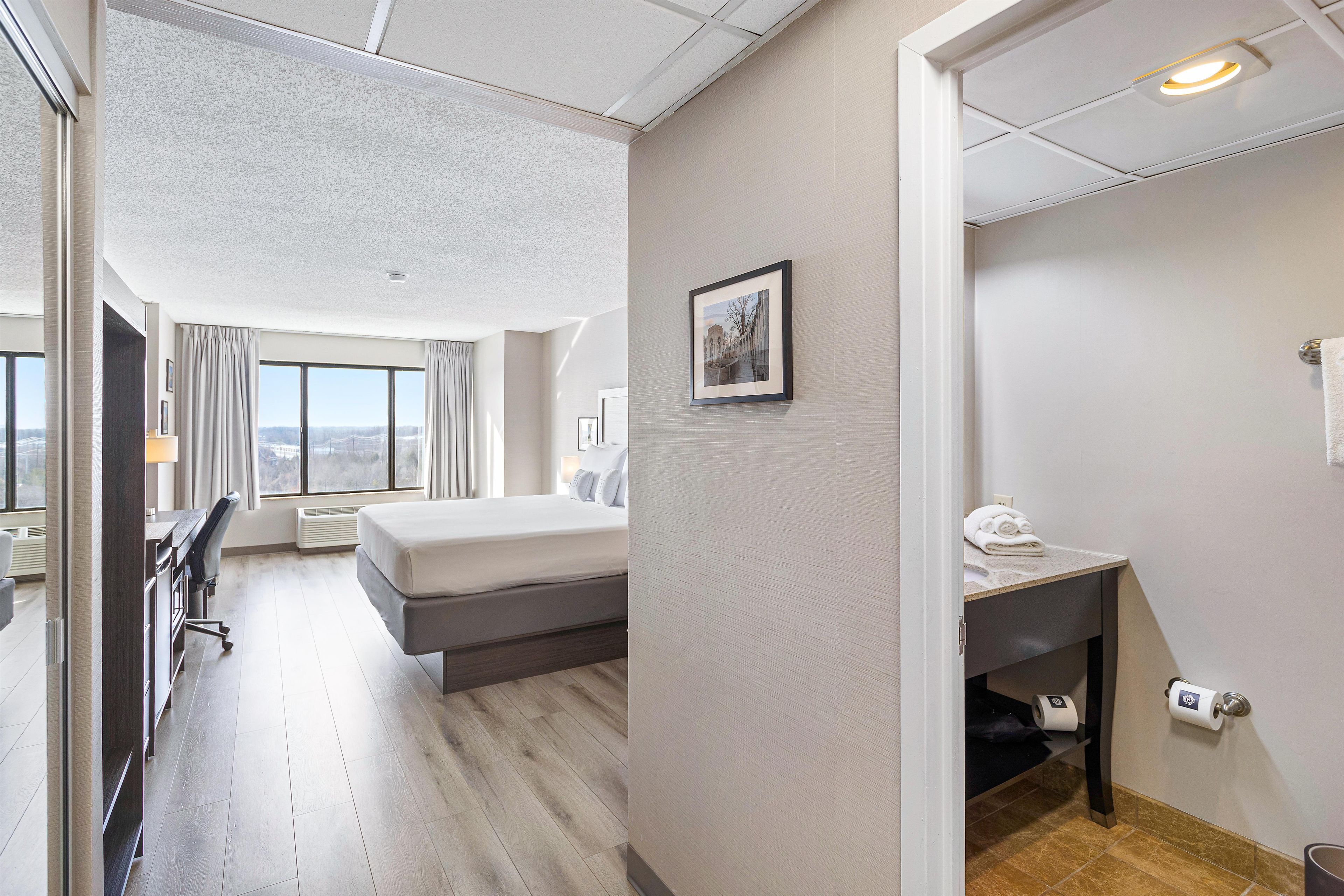 Une chambre d’hôtel comprenant un lit, un bureau, une chaise, un tableau au mur et une salle de bain avec des toilettes et un porte-serviettes.