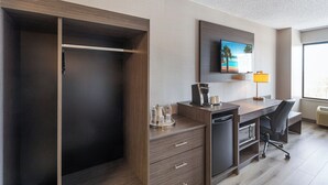 Habitación de hotel con armario, escritorio y silla, cafetera y televisor en la pared.