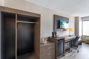 Habitación de hotel con armario, escritorio y silla, cafetera y televisor en la pared.