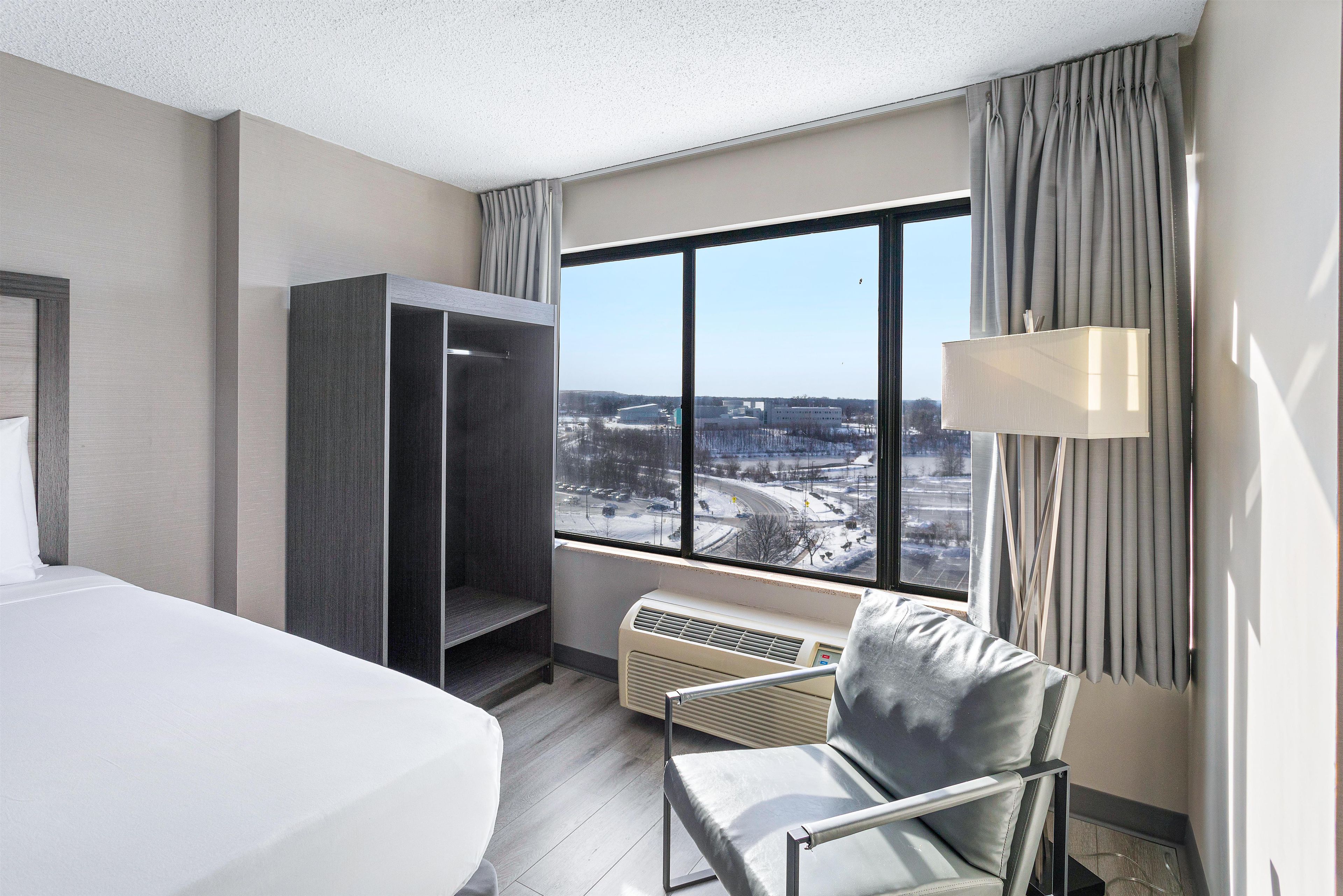 Habitación de hotel con cama, una silla, armario, ventana con vista a un paisaje nevado y lámpara.