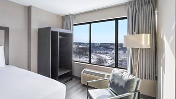 A hotel room with a bed, a chair, a wardrobe, a window with a view of a snowy landscape, and a lamp.