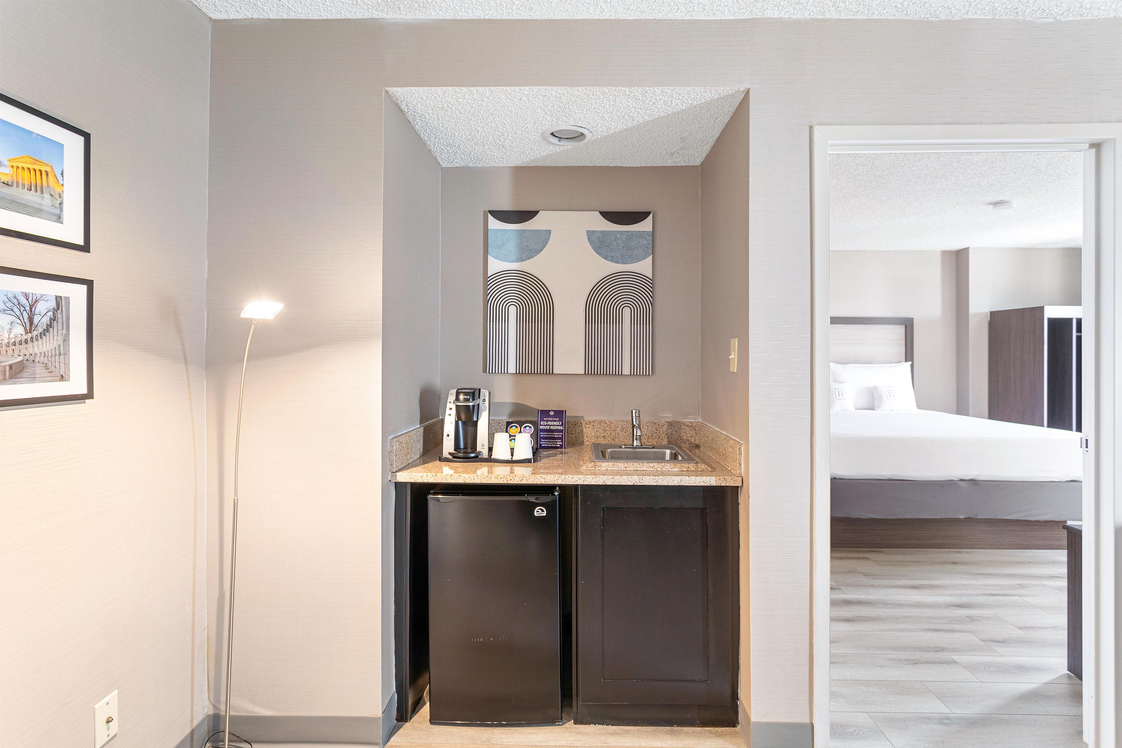 A compact hotel bathroom with a sink, a coffee machine, and a refrigerator.