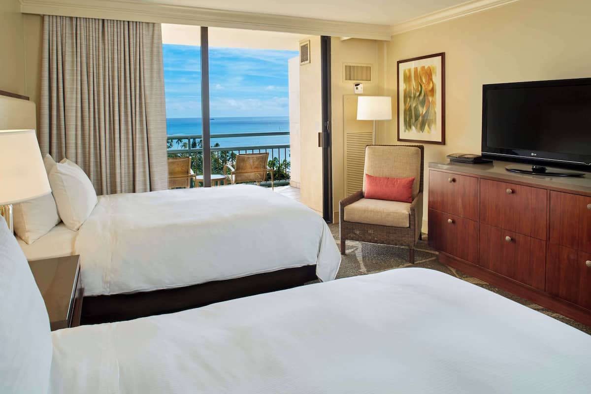 Habitación de hotel con dos camas, televisión, una silla y vista al océano.
