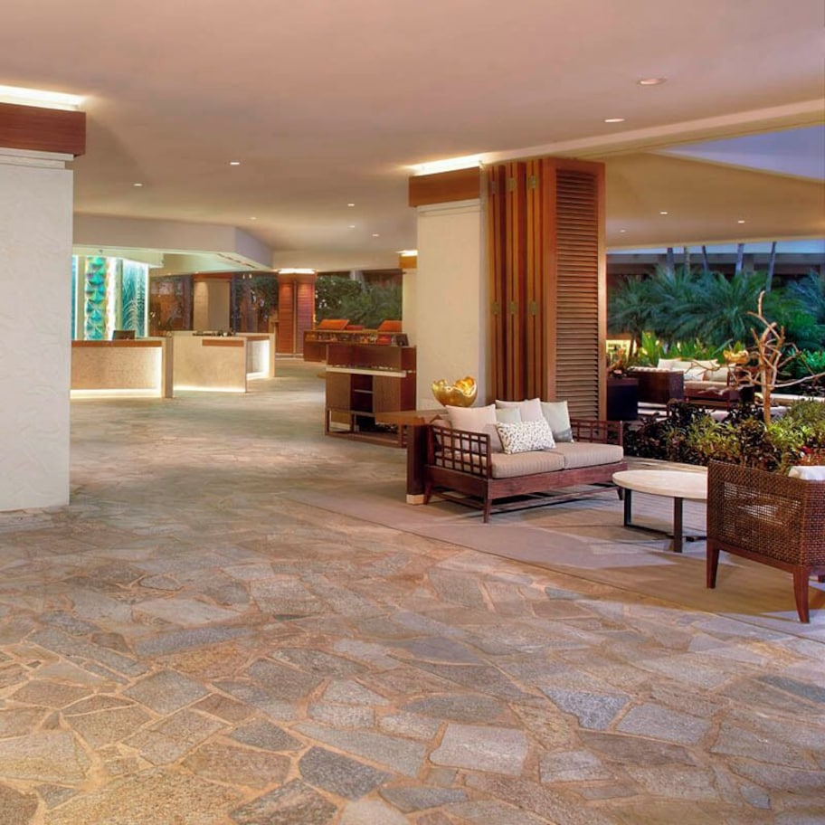 A spacious lobby with stone flooring, a reception desk, seating area, and a view of the outdoors.