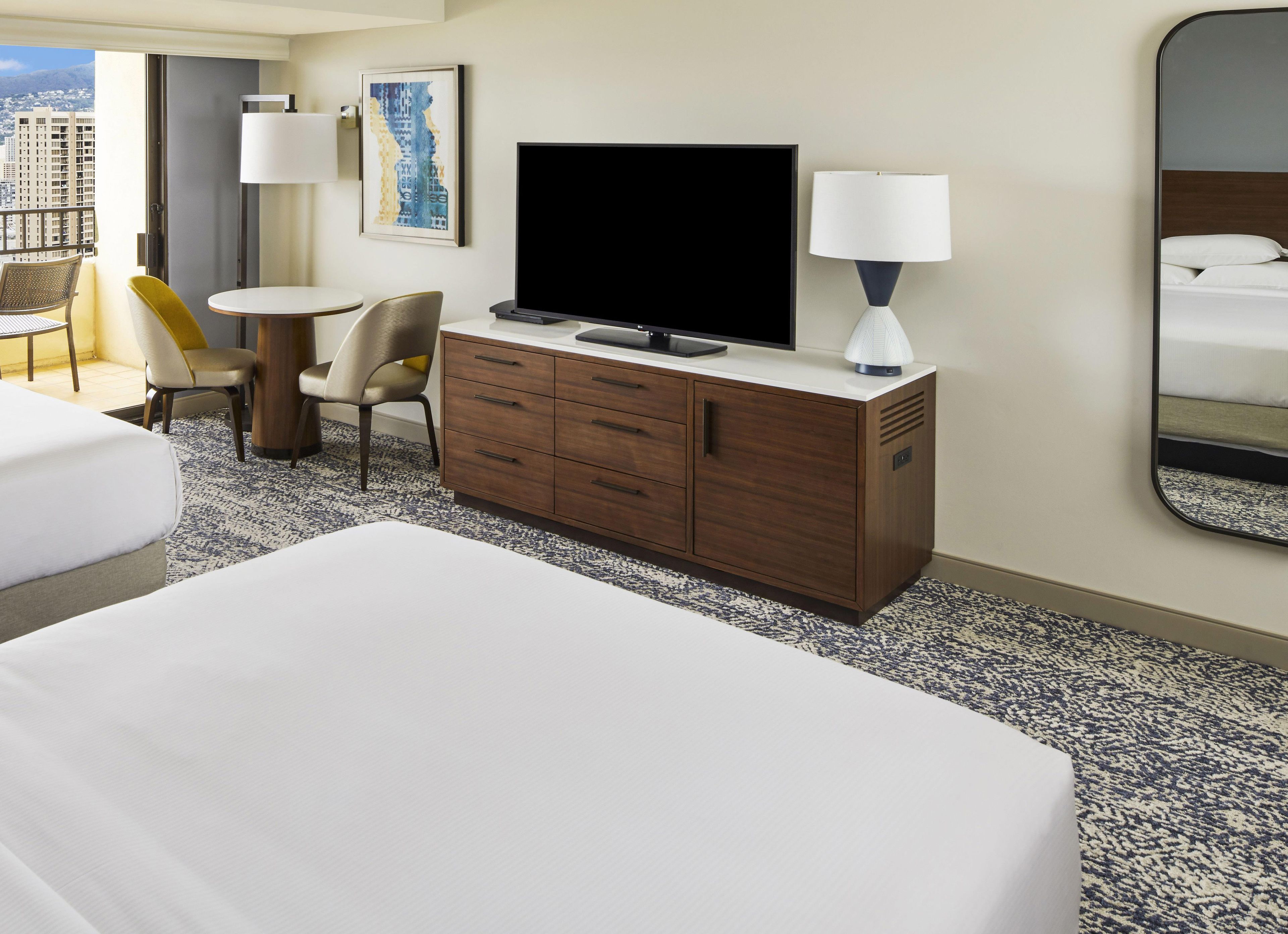 A hotel room with a bed, a desk with a chair, a television, and a mirror.