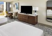 A hotel room with a bed, a desk with a chair, a television, and a mirror.