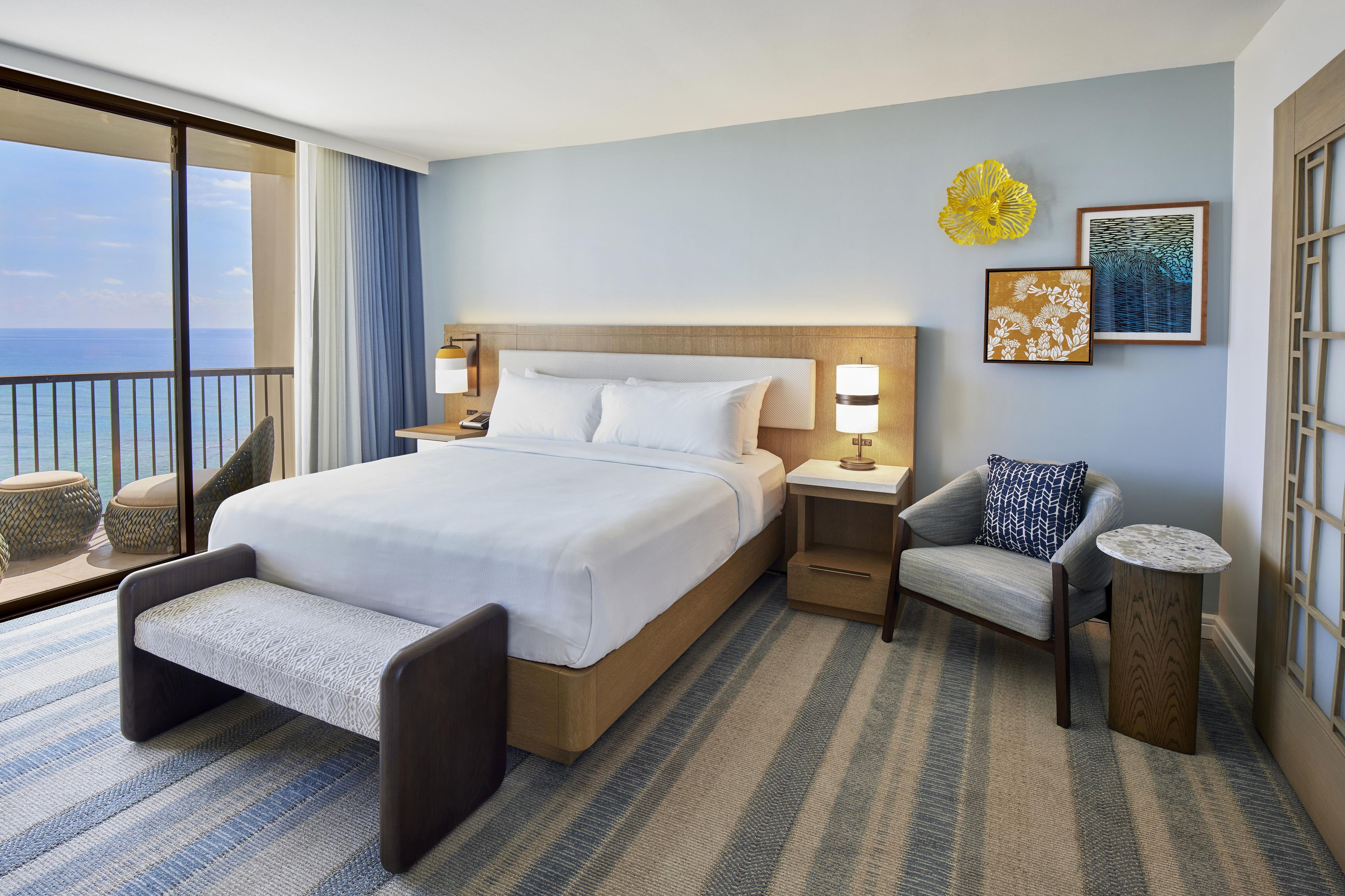 Habitación de hotel con una cama grande, zona de estar, una mesita y vista al mar.