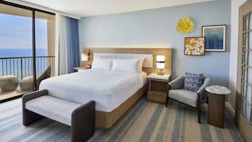 Habitación de hotel con una cama grande, zona de estar, una mesita y vista al mar.