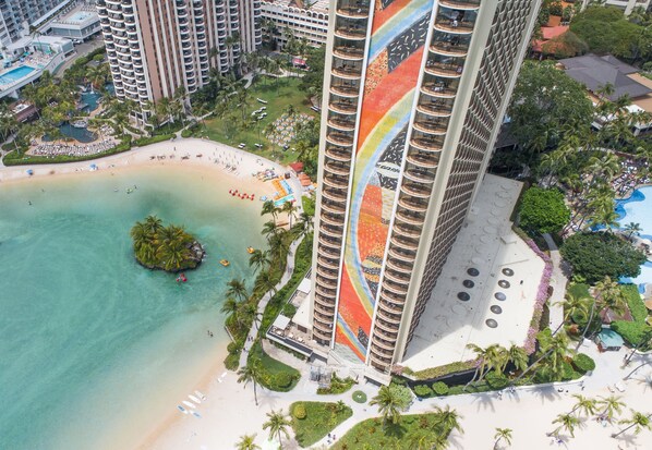 Un hôtel de grande hauteur offrant une vue sur la plage, doté de nombreux balcons et d’un espace piscine.