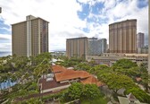 A high-rise hotel with multiple balconies, surrounded by lush greenery and a view of the ocean.