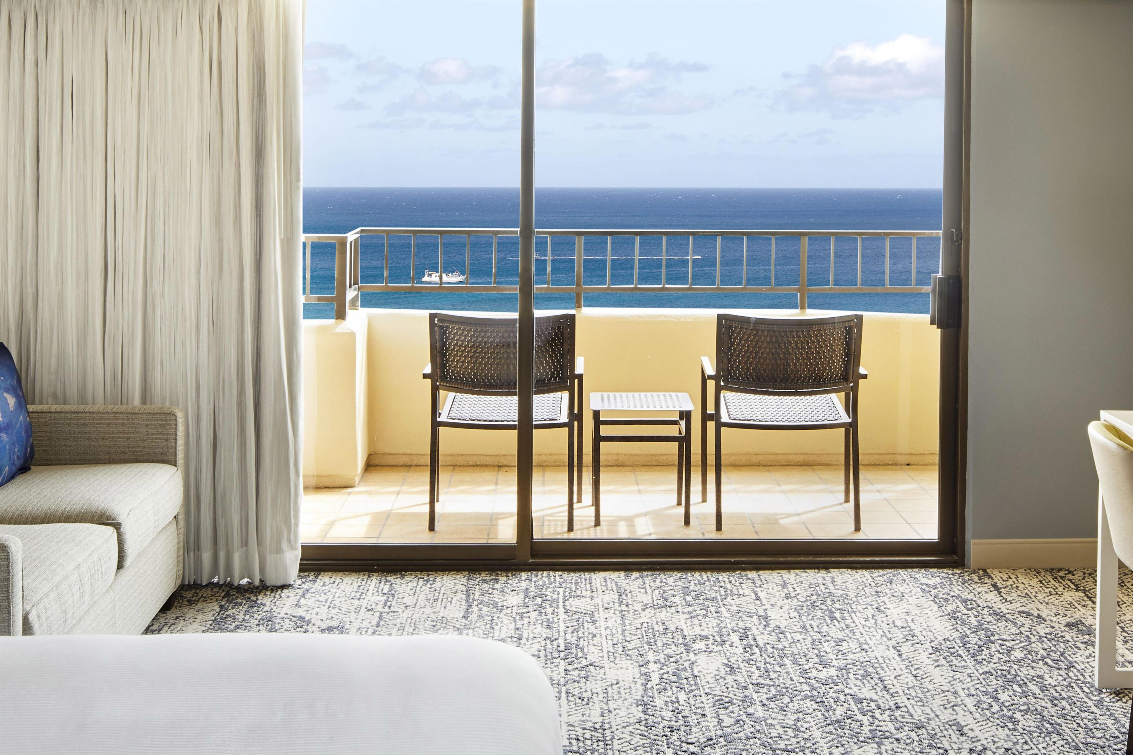 A hotel room with a balcony, two chairs, a small table, and a view of the ocean.