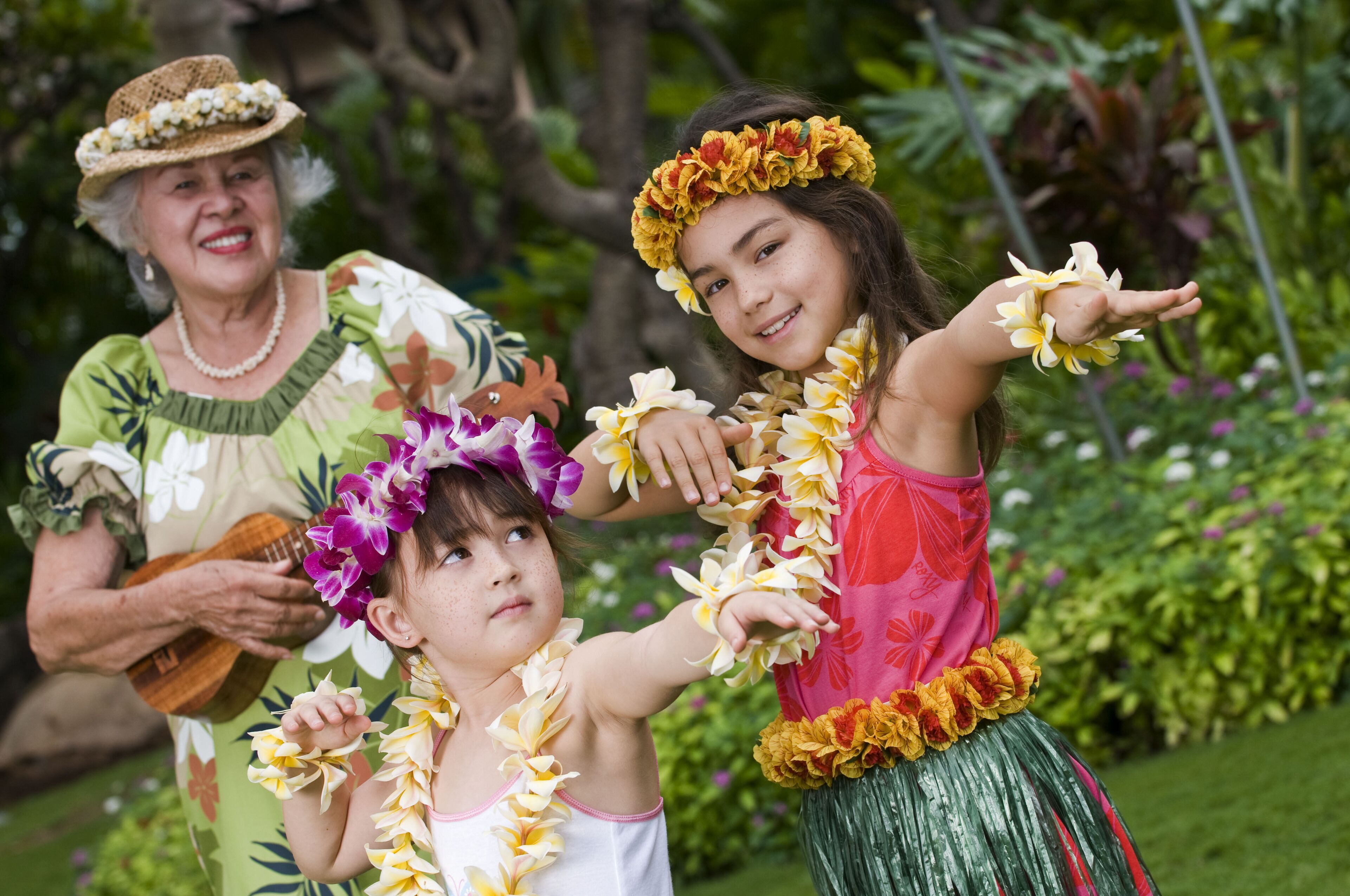 A person playing a ukulele, another holding a lei, and a third with a lei around their neck.
