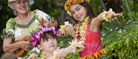 A person playing a ukulele, another holding a lei, and a third with a lei around their neck.