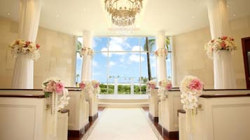 A wedding aisle with floral decorations, a chandelier, and a view of the beach.