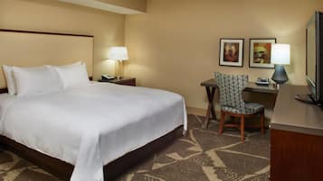 A hotel room with a large bed, a desk with a chair, two wall-mounted lamps, and two framed pictures.