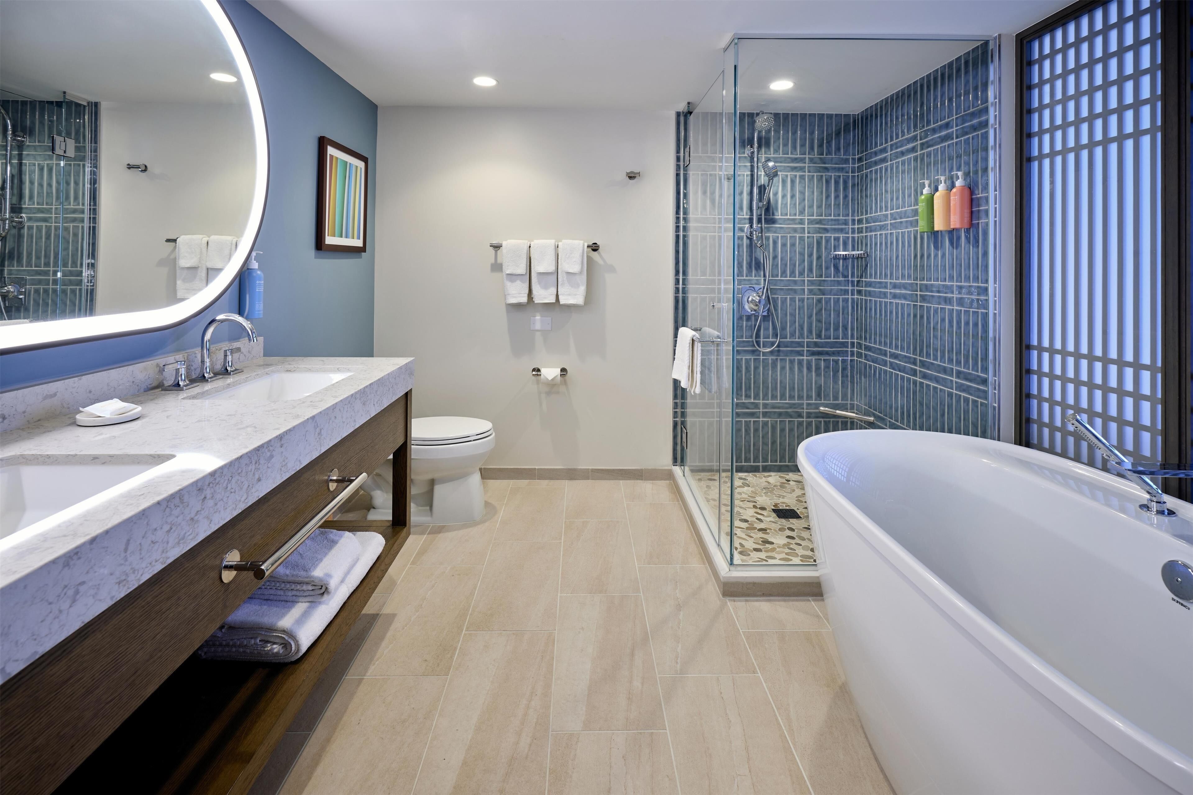 Een moderne badkamer met een grote spiegel, twee wastafels, een toilet en een douche met glazen deuren.