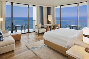 Habitación de hotel con una cama grande, una zona de estar con mesa y sillas, y un balcón con vistas al océano.