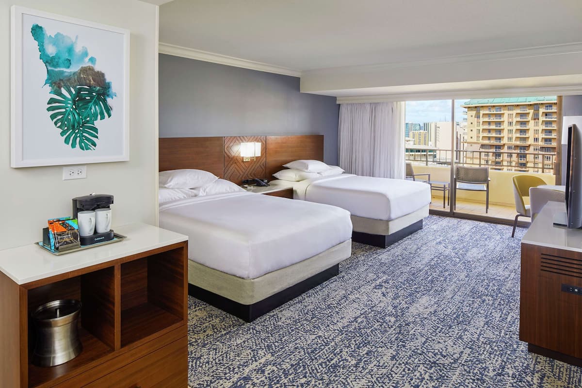 Habitación de hotel con dos camas, minibar, escritorio, silla y un gran ventanal con vistas a la ciudad.