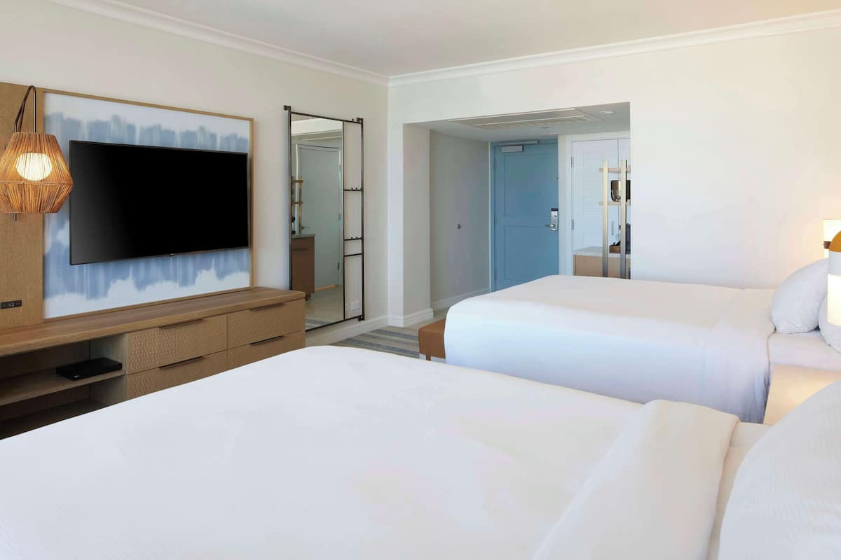 Habitación de hotel con dos camas, televisión, cómoda de madera y espejo.