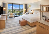 A hotel room with a large bed, a TV, a balcony with a city view, and a breakfast bar.