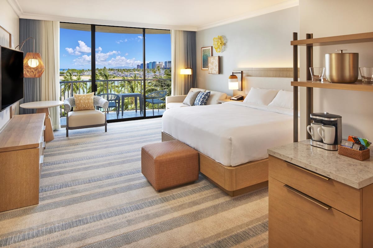 Habitación de hotel con una cama grande, televisión, balcón con vistas a la ciudad y desayunador.