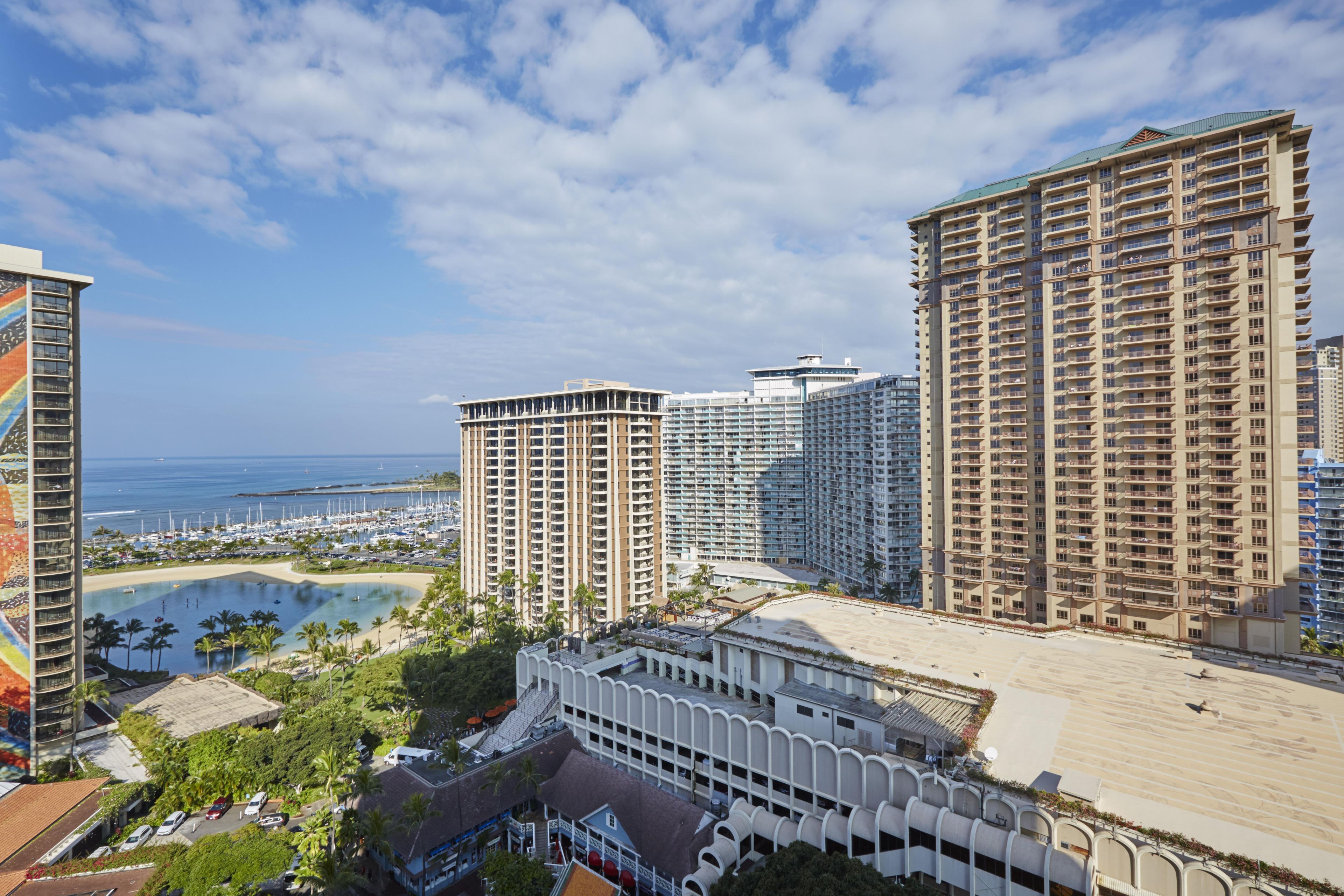 A high-rise hotel with multiple balconies, a marina with boats, and a beach area.