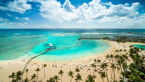 Una playa con aguas turquesas cristalinas, un muelle y palmeras.