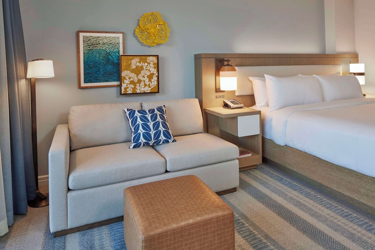A hotel room with a sofa, a bed, a nightstand, and a lamp.