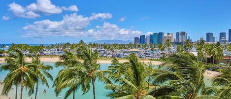 A coastal cityscape with a beach, palm trees, and a marina.