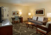 A hotel room with a sofa, two armchairs, a coffee table, a desk with a chair, a television, and two lamps.