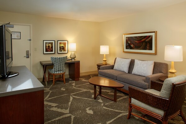 A hotel room with a sofa, two armchairs, a coffee table, a desk with a chair, a television, and two lamps. - Hilton Hawaiian Village Waikiki Beach Resort (Honolulu)