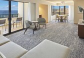 A hotel room with a balcony, a dining area, and a seating area with a view of the cityscape.