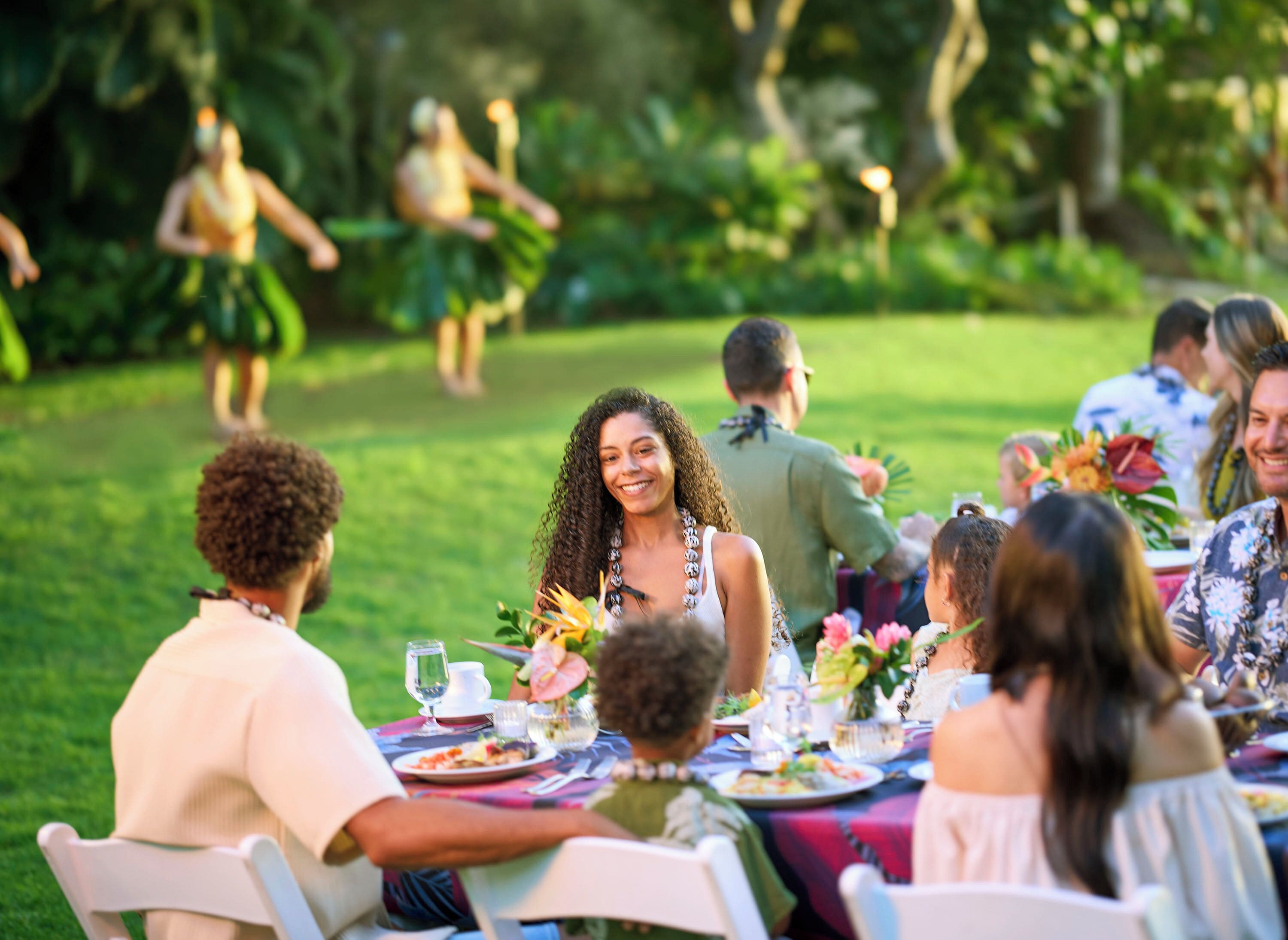 A group of people seated at an outdoor dining table with a view of a garden.