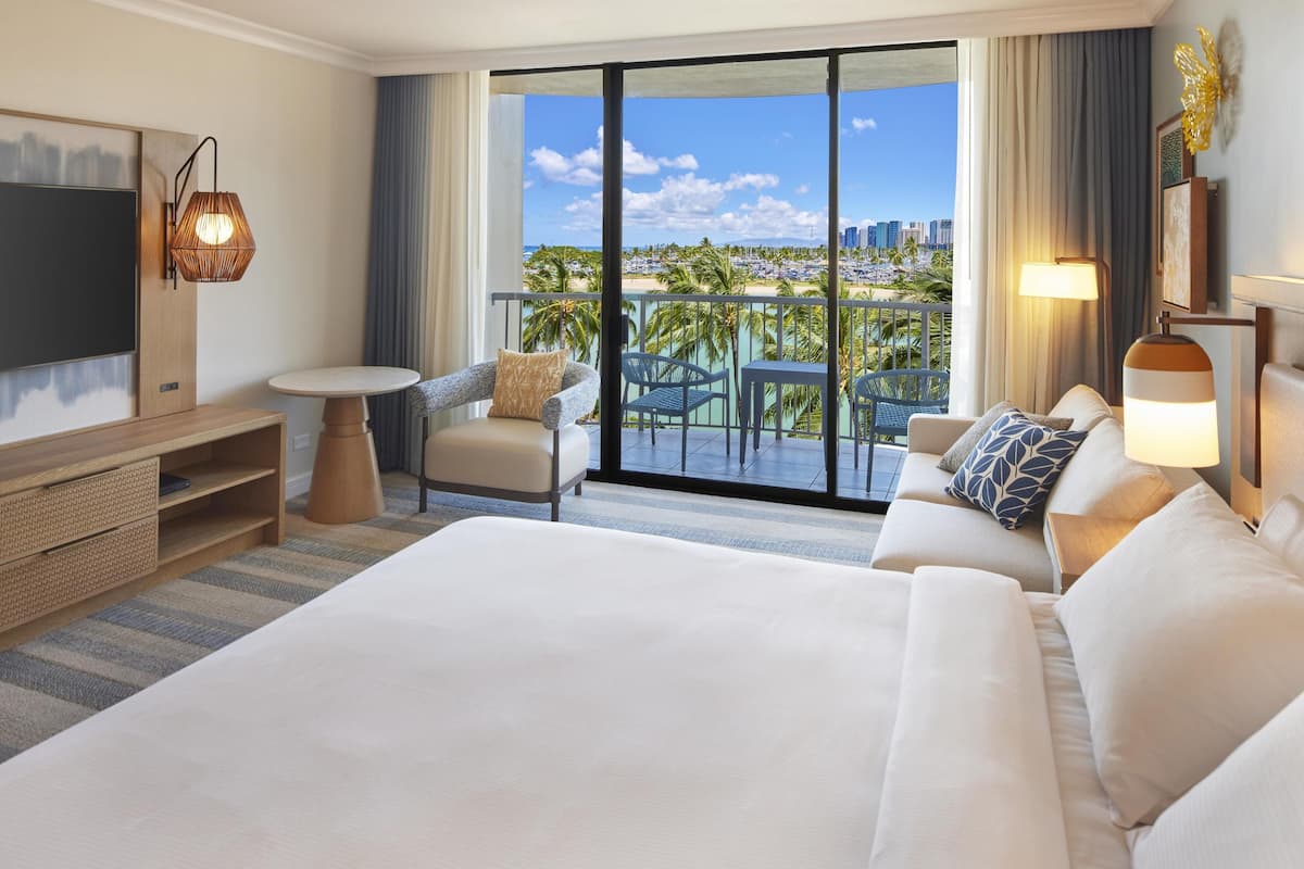 Una habitación de hotel con una cama grande, televisión, balcón con vistas a la ciudad y zona de comedor.