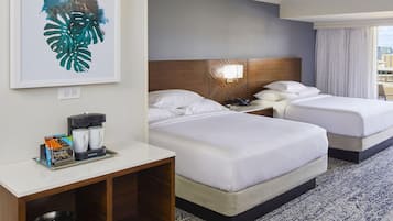 Habitación de hotel con dos camas, una mesita de noche con cafetera, una obra de arte enmarco y vistas a la ciudad.