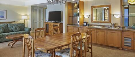 A hotel room with a dining area, a sofa, a television, and a kitchen with a sink and cabinets.