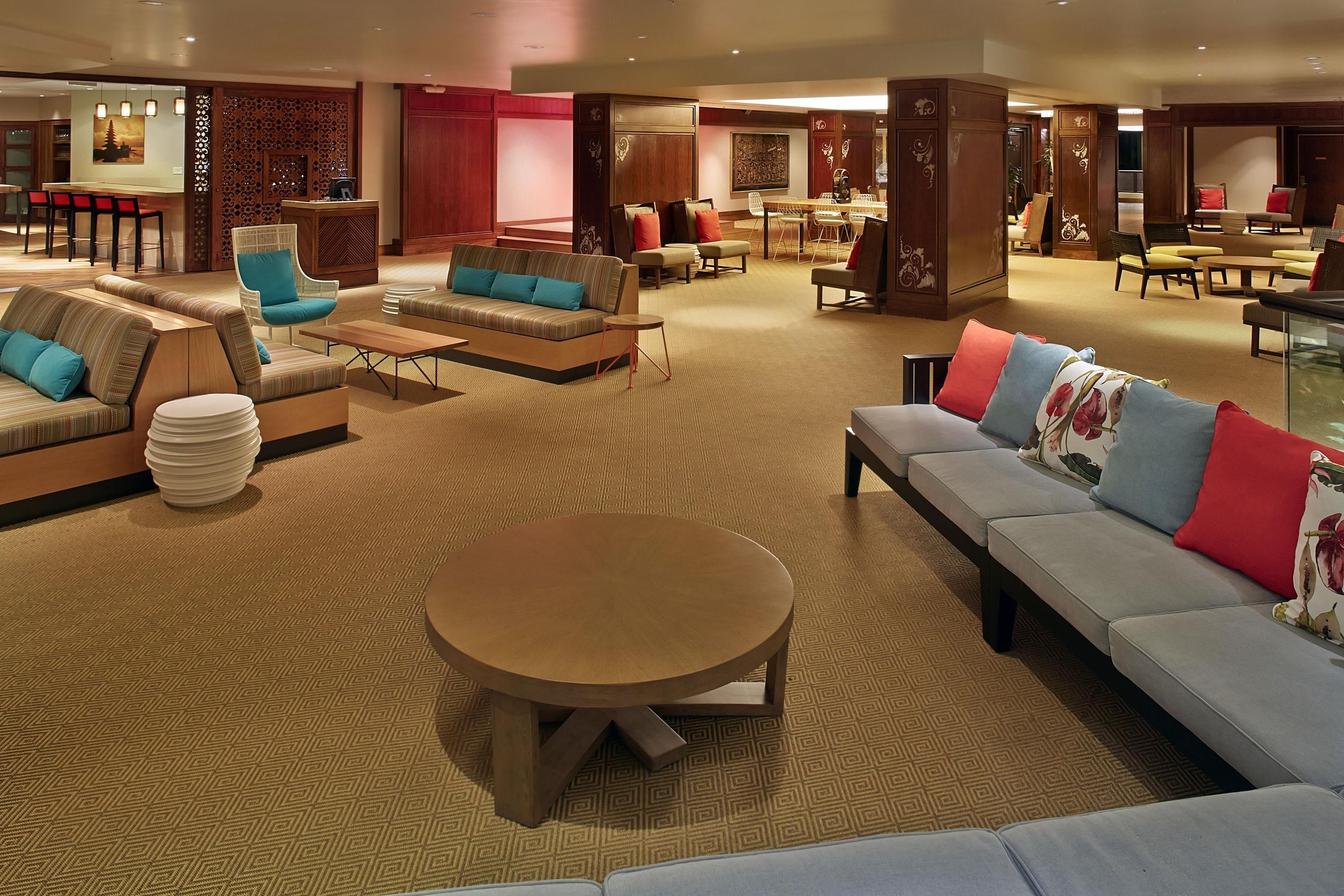 Un amplio vestíbulo de hotel con varias zonas de estar, incluyendo sofás y sillones, una mesa redonda central y un comedor con una mesa larga y sillas.