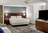 A hotel room with a bed, bedside tables, a television, and a dresser.
