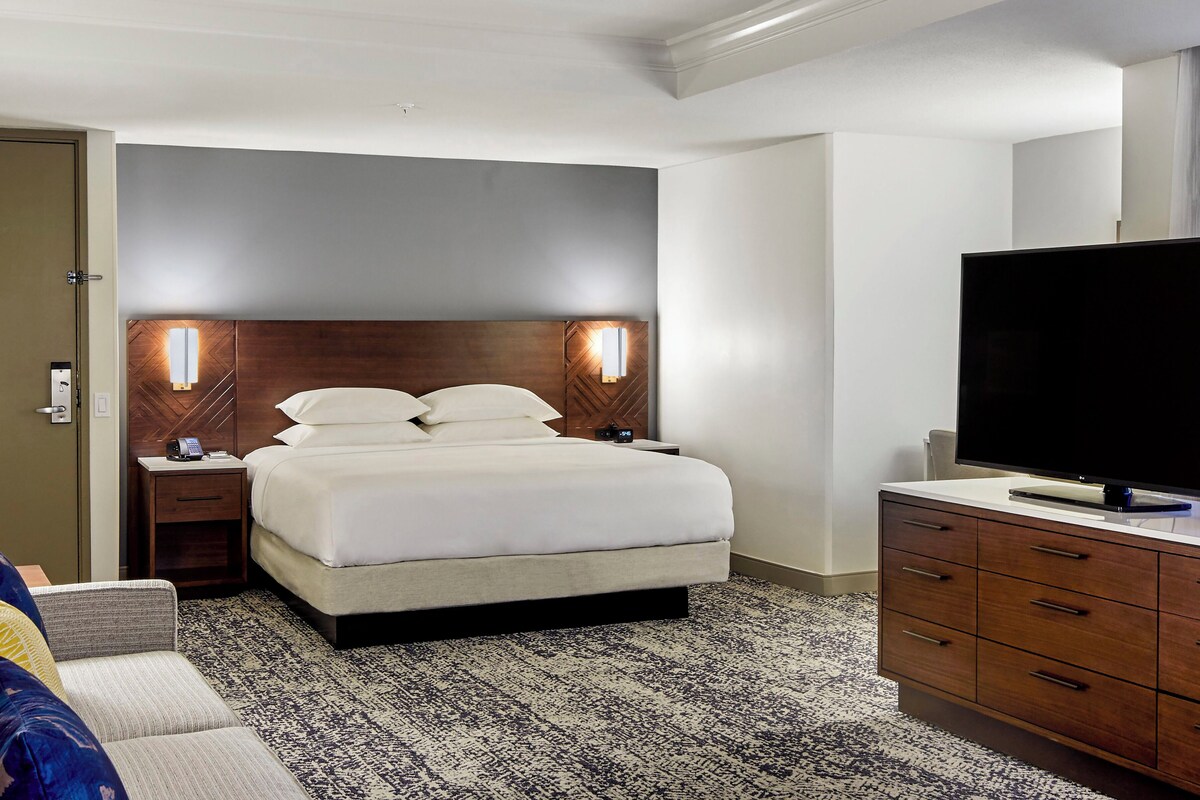 A hotel room with a bed, bedside tables, a television, and a dresser.