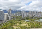 A cityscape with high-rise buildings, a park with palm trees, and mountains in the background.