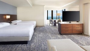 A hotel room with a large bed, a desk with a TV, and a view of the ocean.